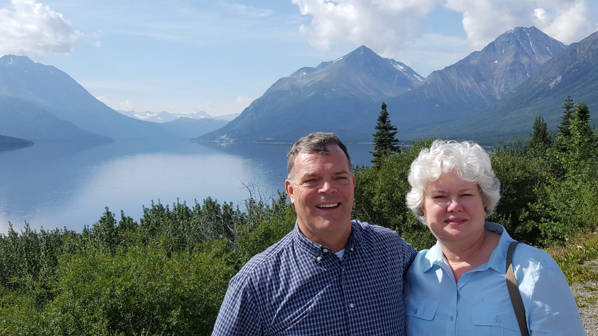 Couple smiling with mountain lake background.