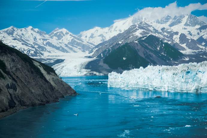 Snowy mountains and glacier by blue water.