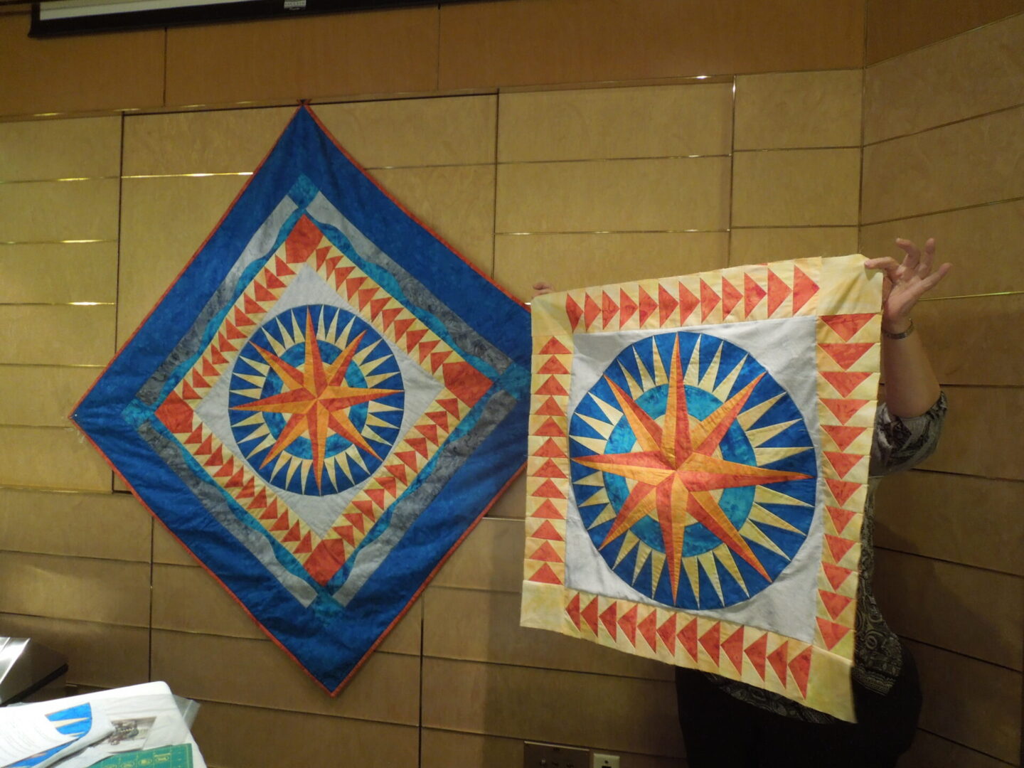 Two colorful quilt patterns displayed on wall.