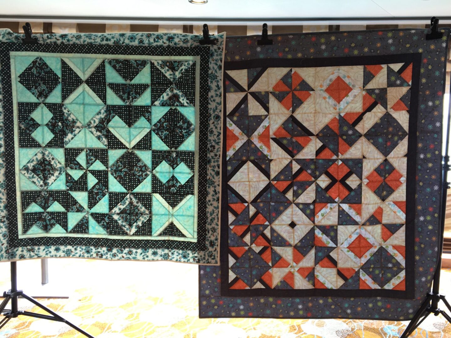 Two geometric pattern quilts on display stands.