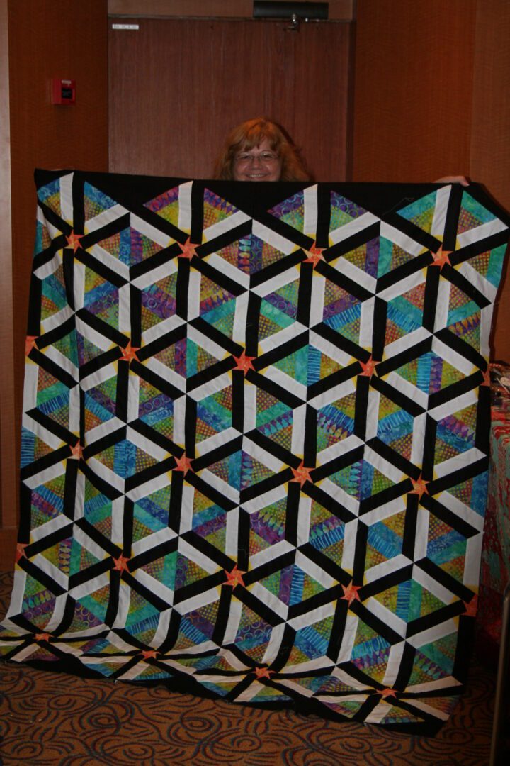 Person holding colorful geometric quilt indoors.