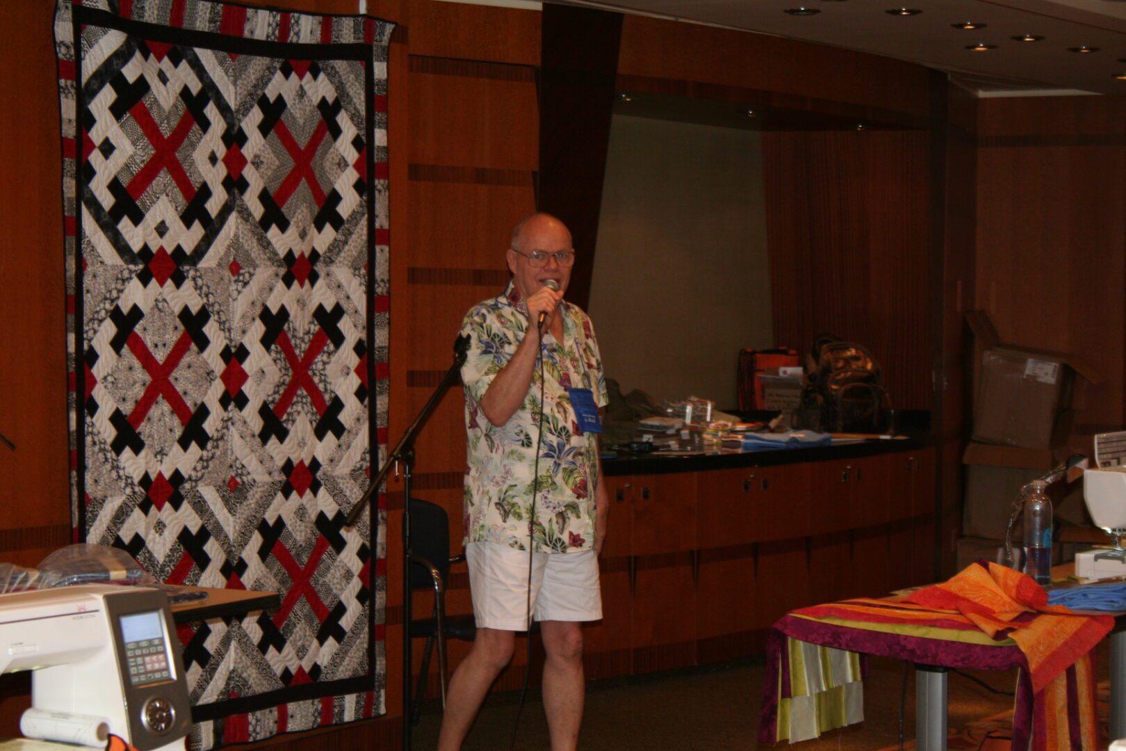 Man speaking near a quilt on display.