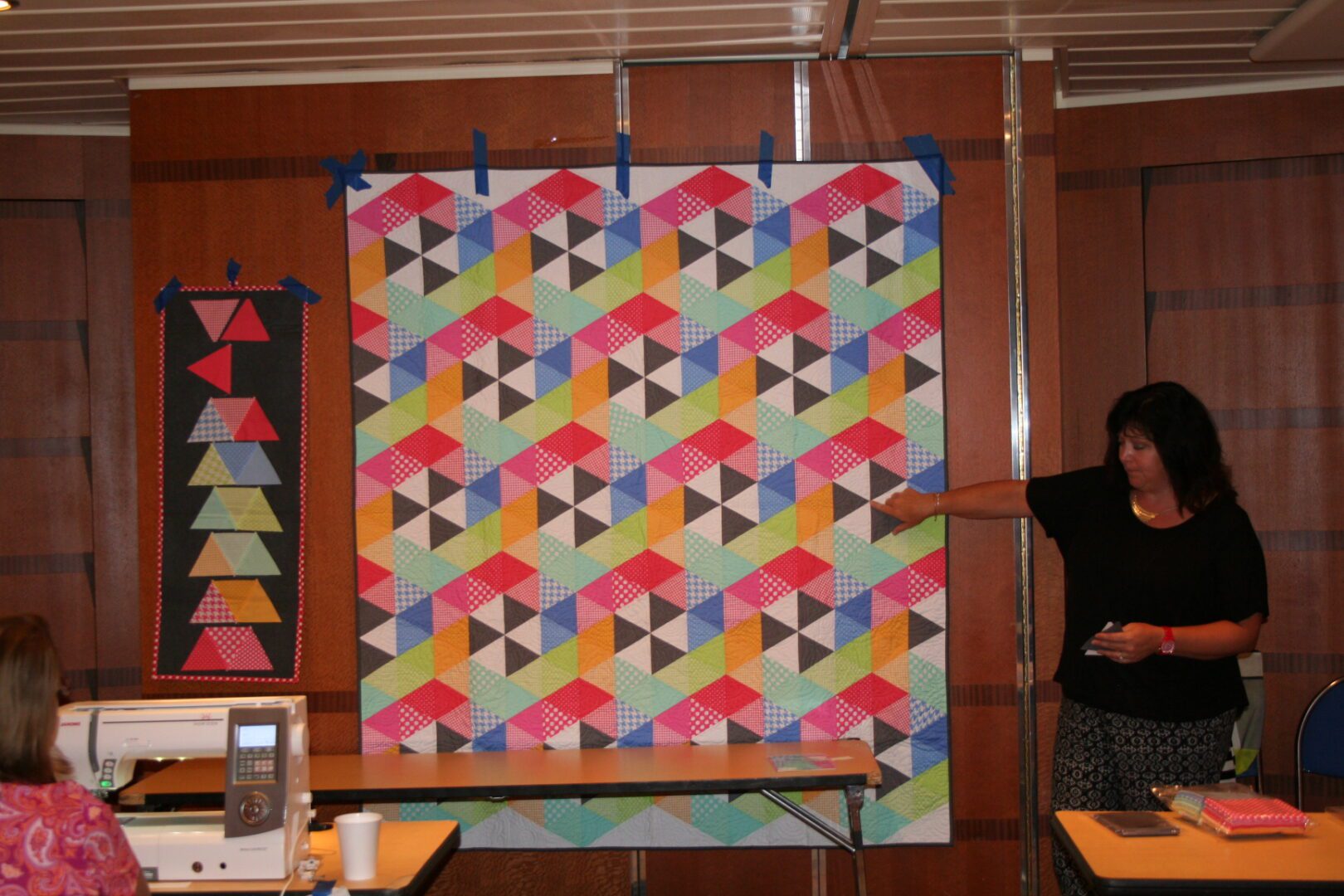 Woman presenting colorful geometric quilt pattern.